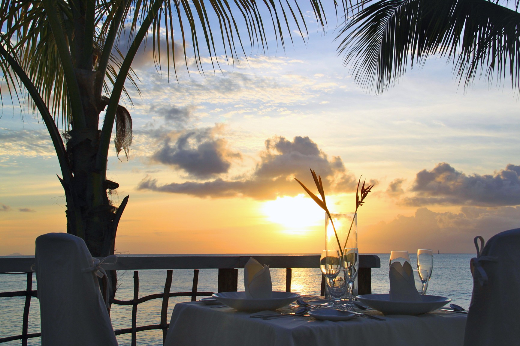 a table with glasses and plates on it by a palm tree and a sunset